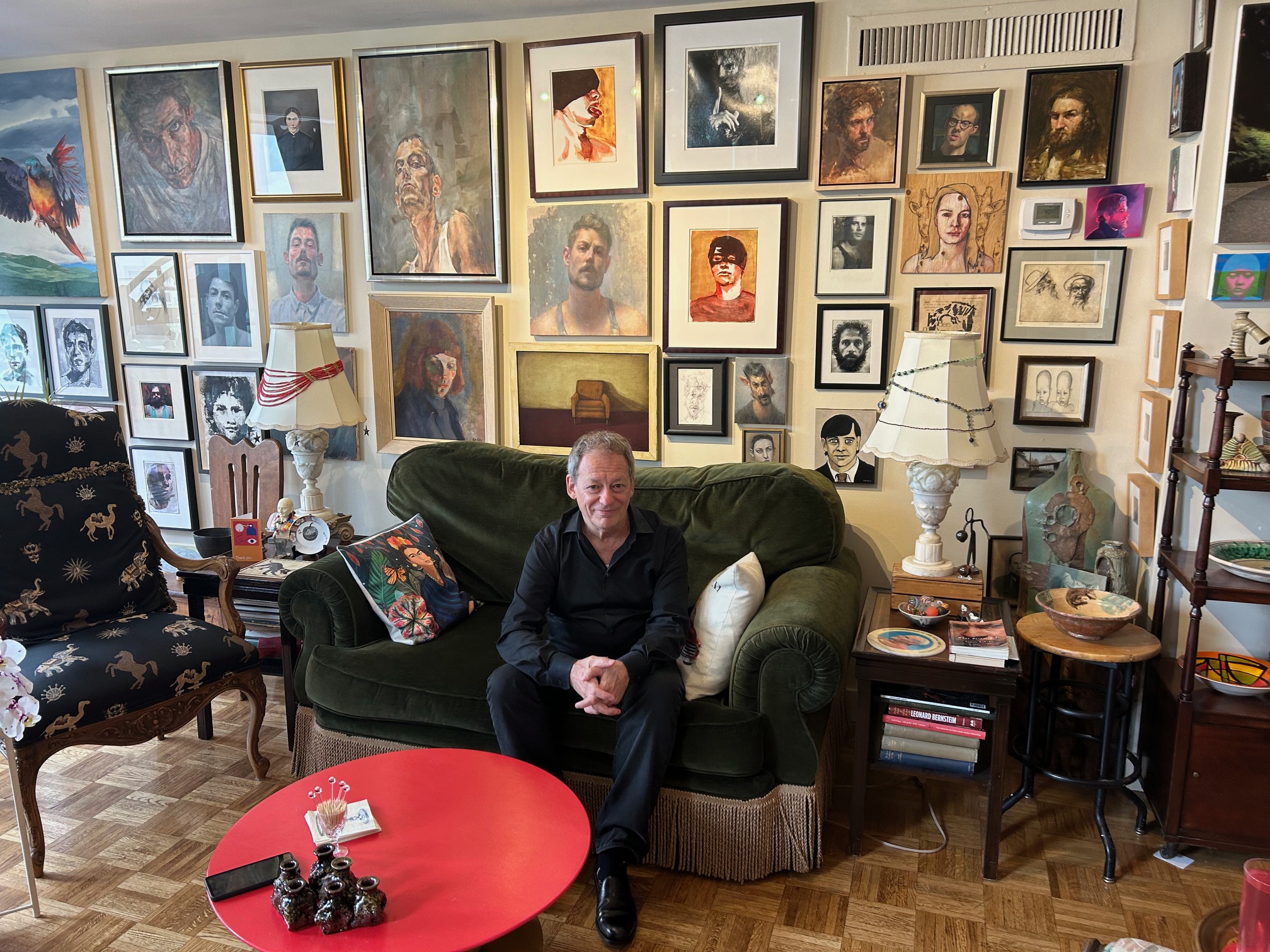 Flavio Belli sitting in his living room in front of his wall of strategically placed portraits